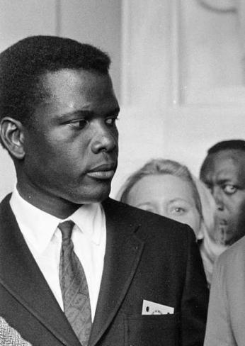 African-American Actor Sidney Poitier standing in front of the Lincoln Monument, wearing a dapper suit with a stoic look on his face.