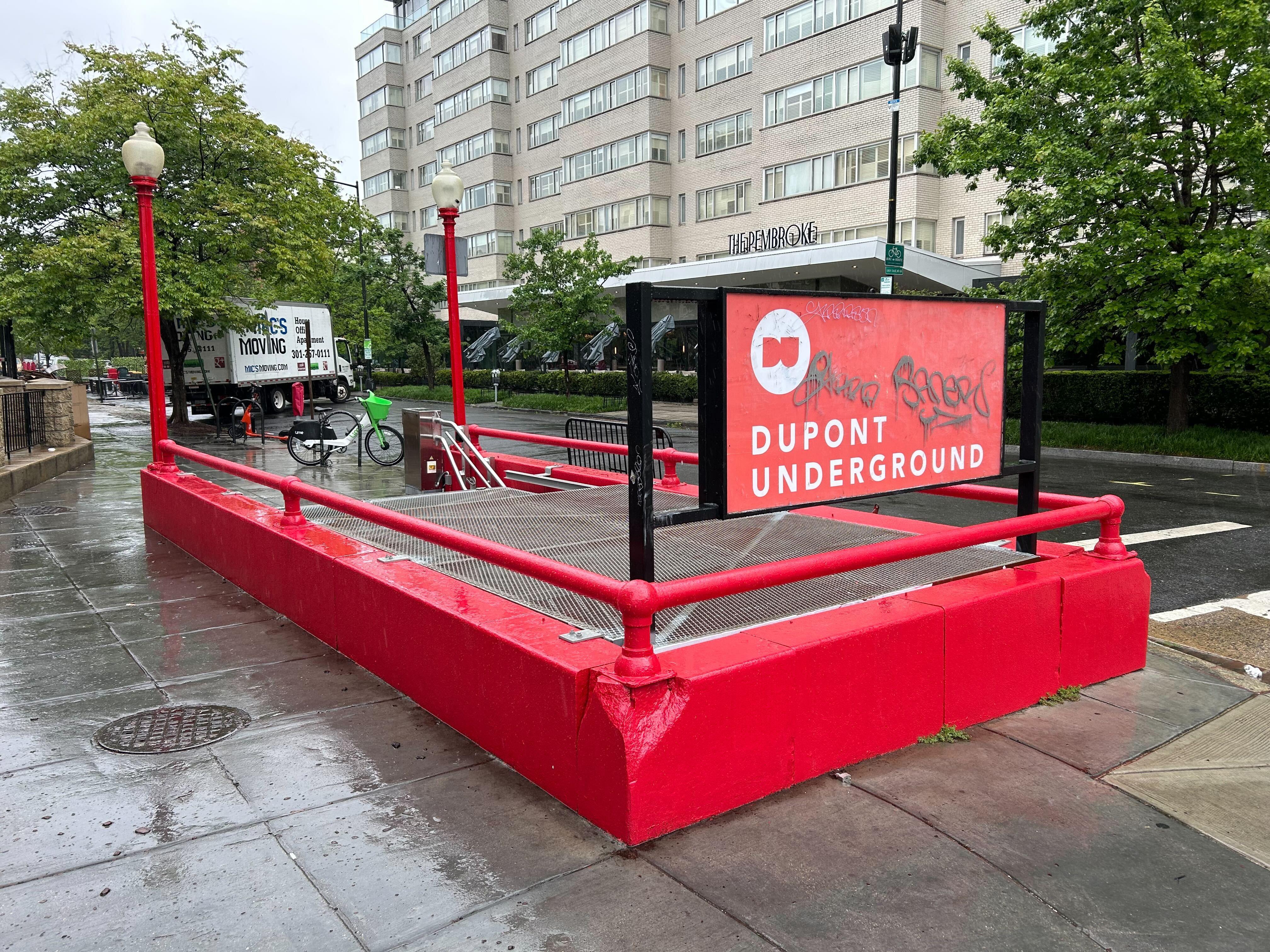 A short red concrete edge surrounds a staircase leading below Dupont Circle. A green sign reads "Dupont Underground."