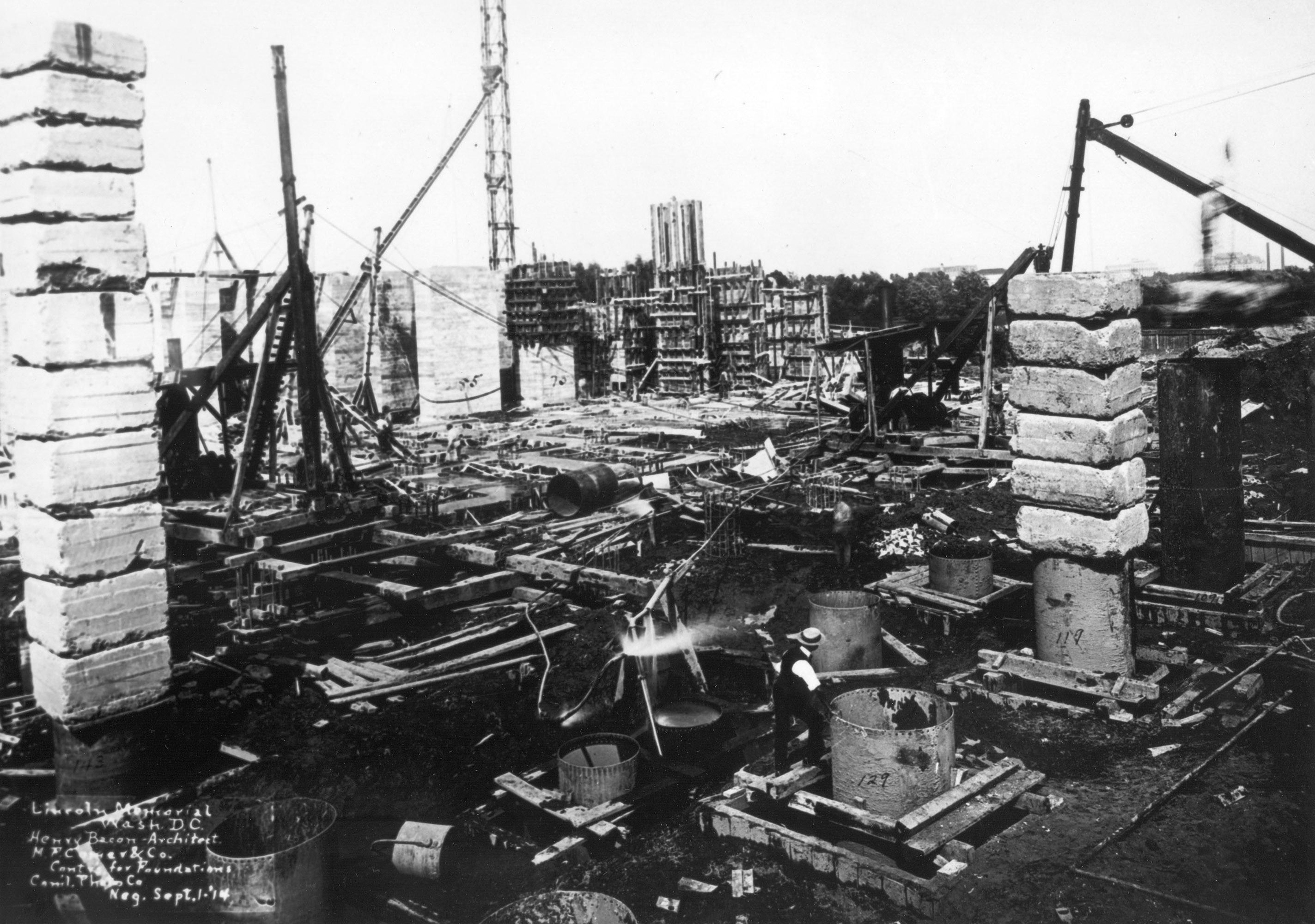 The final structural design called for sub-foundations of reinforced concrete poured into cylindrical steel piers driven through the unstable fill to bedrock 65 feet below. Upper foundations of concrete columns would support the memorial’s floor, and earth fill would cover these columns to form a terrace around the building. Here, several metal cylinders are in the foreground, some of them topped by heavy weights to help drive them downward