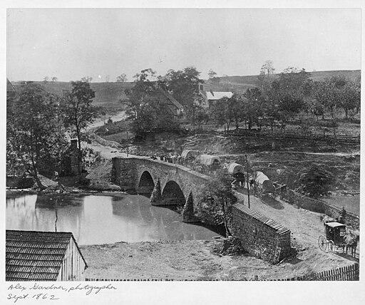 A photo of the Burnside Bridge, in black-and-white. It goes over water and several horse-drawn carriages cross it.