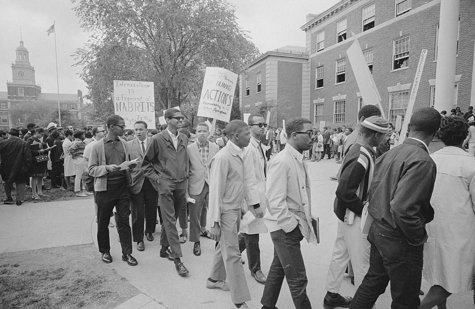 Crowd looks on as group of Howard University students on university campus protest holding picket signs.