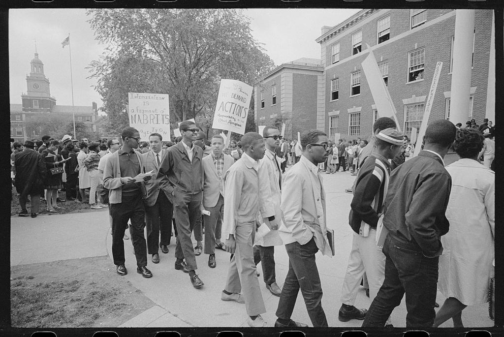 Crowd looks on as group of Howard University students on university campus protest holding picket signs.