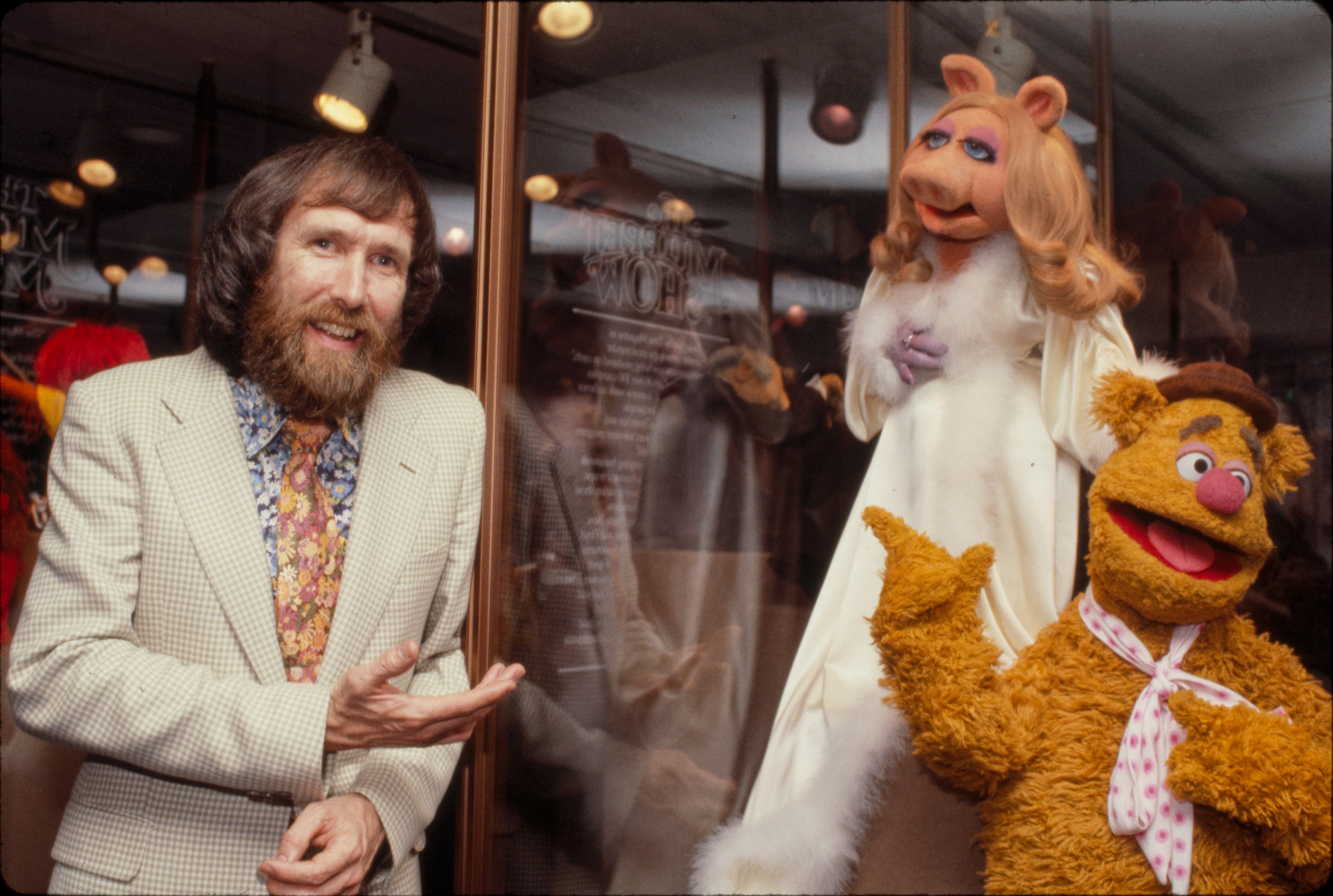 Jim Henson dressed in white suit standing with Miss Piggy and Fozzie Bear