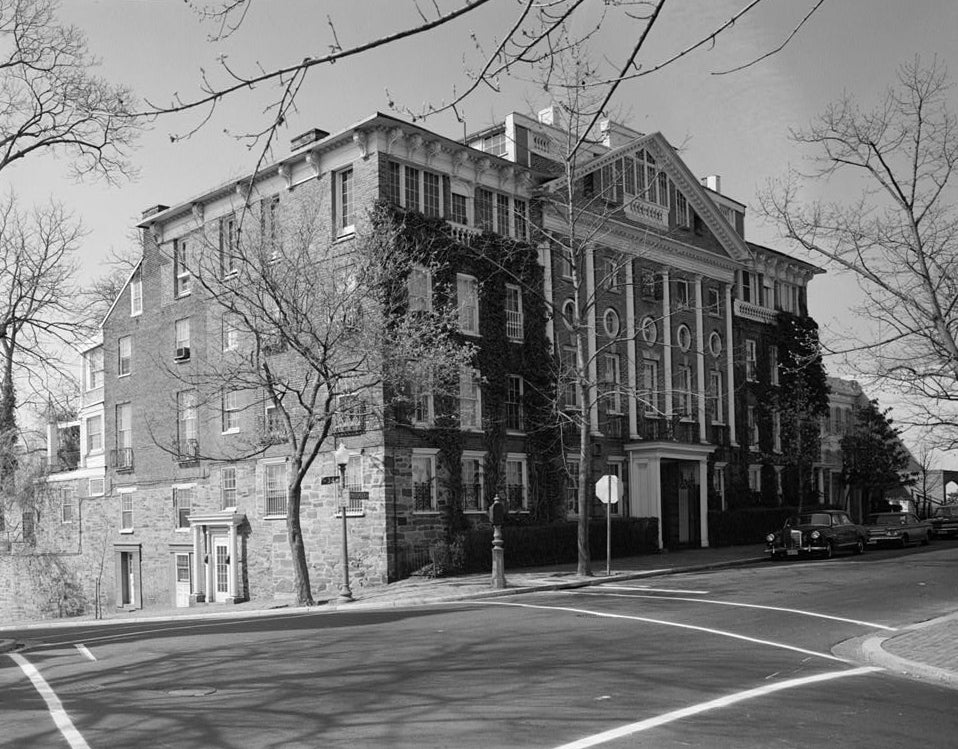 Black and white photo of large brick house with cars in front.