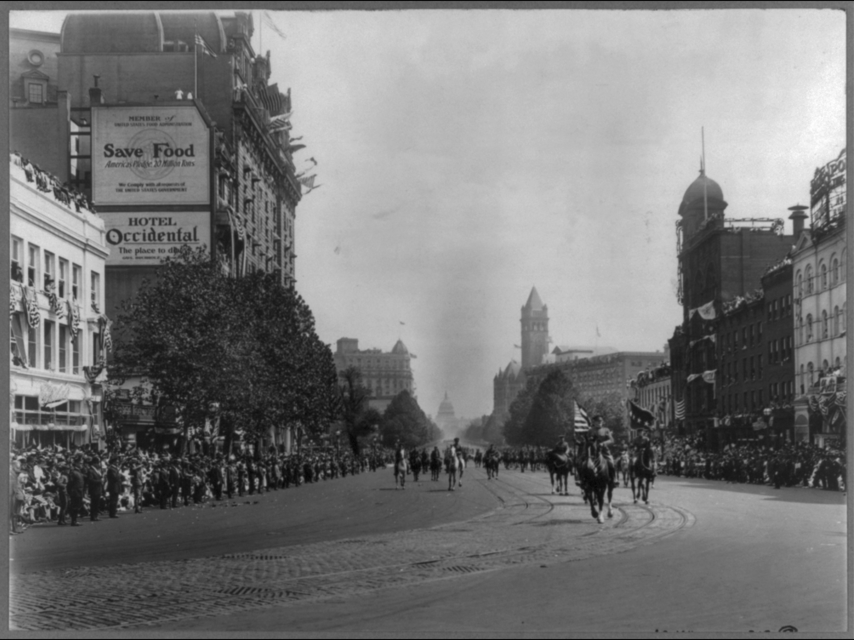 Soldiers walk down a street in DC. Crowds of people line either side of the street.